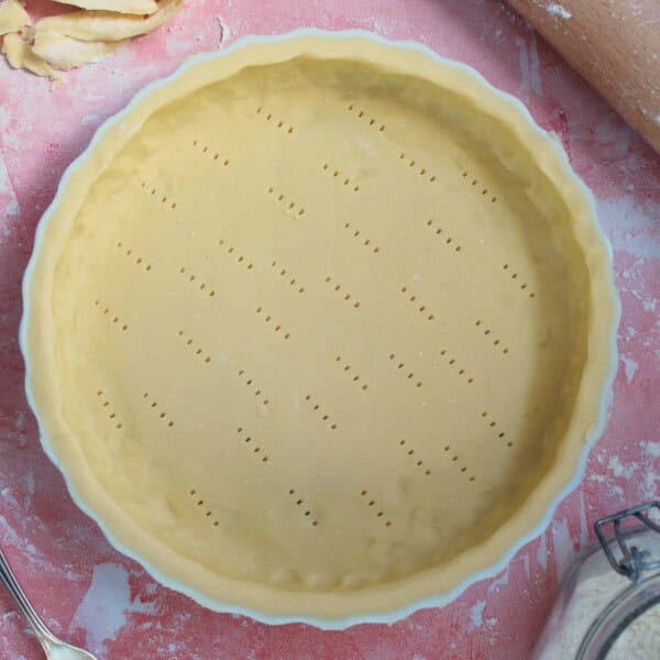 An uncooked pie crust with a rolling pin and gluten free pastry offcuts.