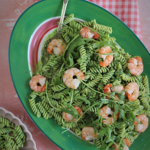 A plate of green pasta sauce with fusilli and prawns.