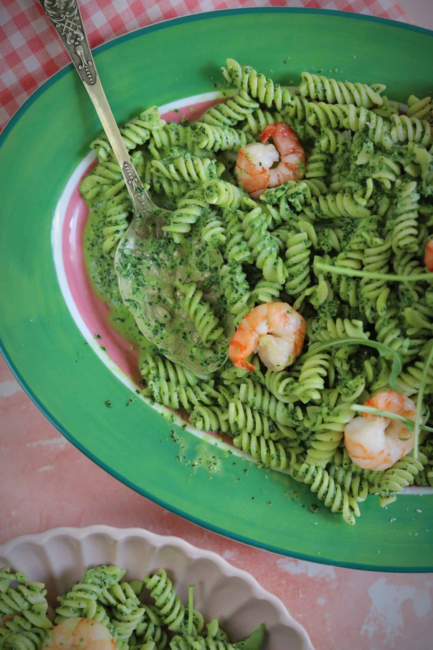 A plate of green pasta sauce with tiger prawns.