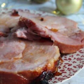 Slices of slow cooker gammon in ginger beer on a festive plate.