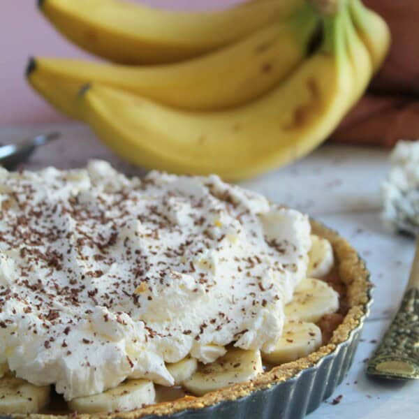 A gluten free banoffee pie with bananas in the background.