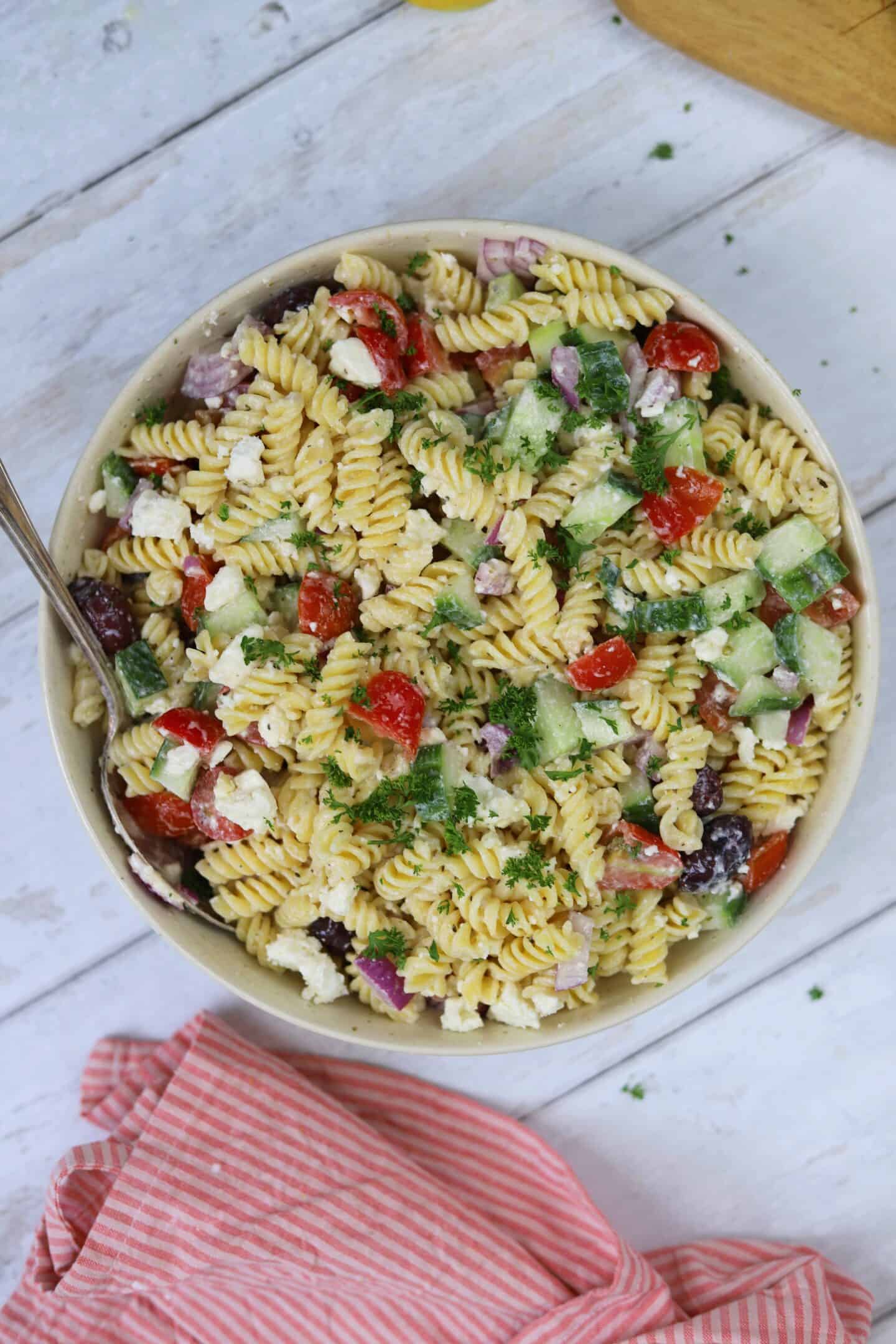 A bowl of Greek pasta salad on a white wooden backdrop.