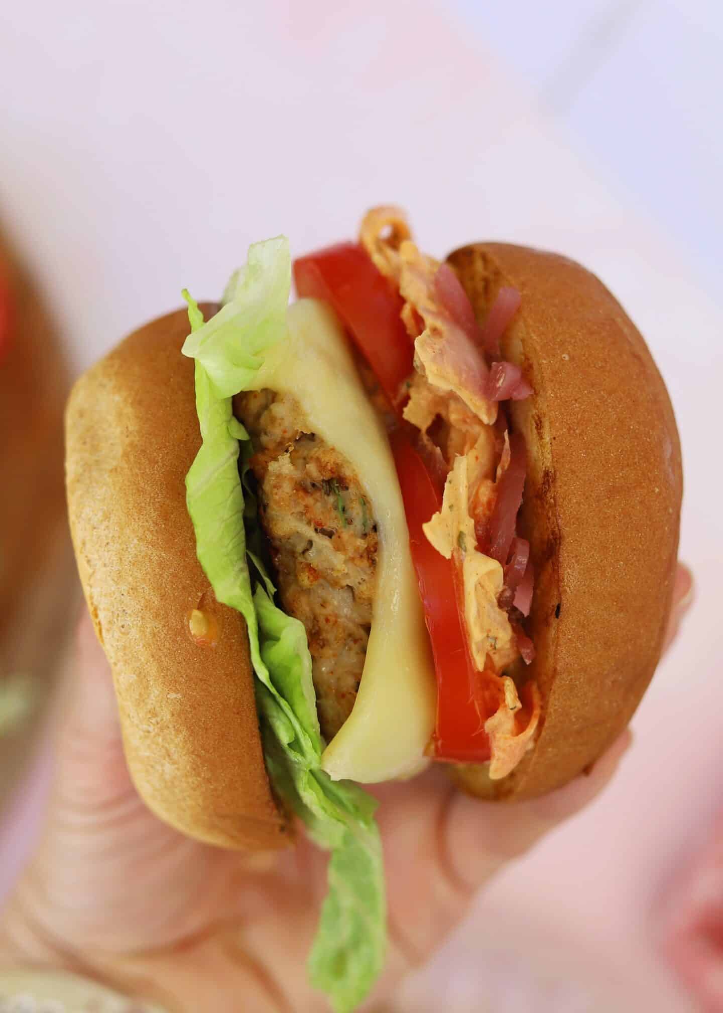 A gluten free ground chicken burger in a bun with lettuce, tomato and cheese.