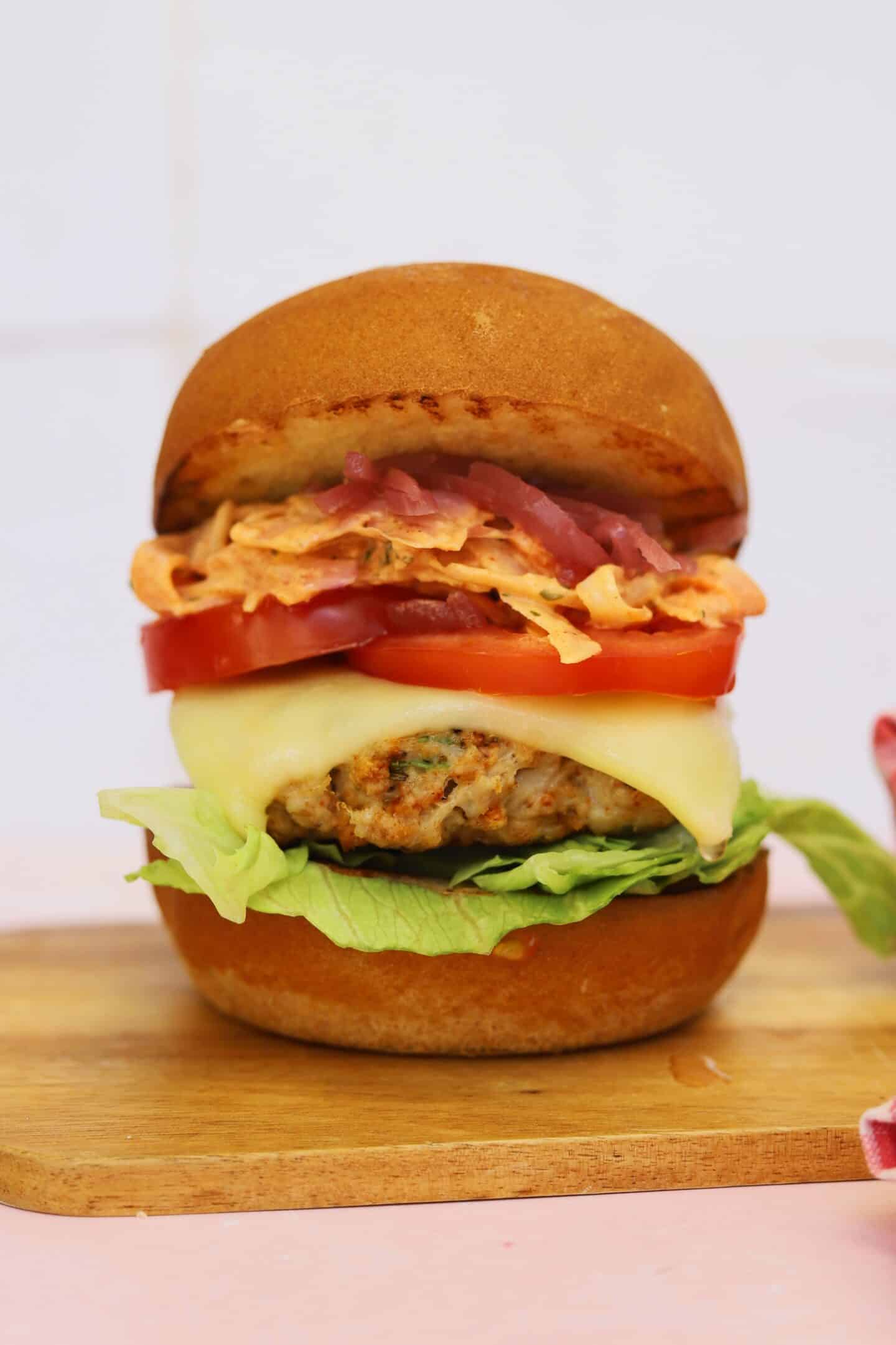 A gluten free ground chicken burger in a bun with lettuce, tomato and cheese.