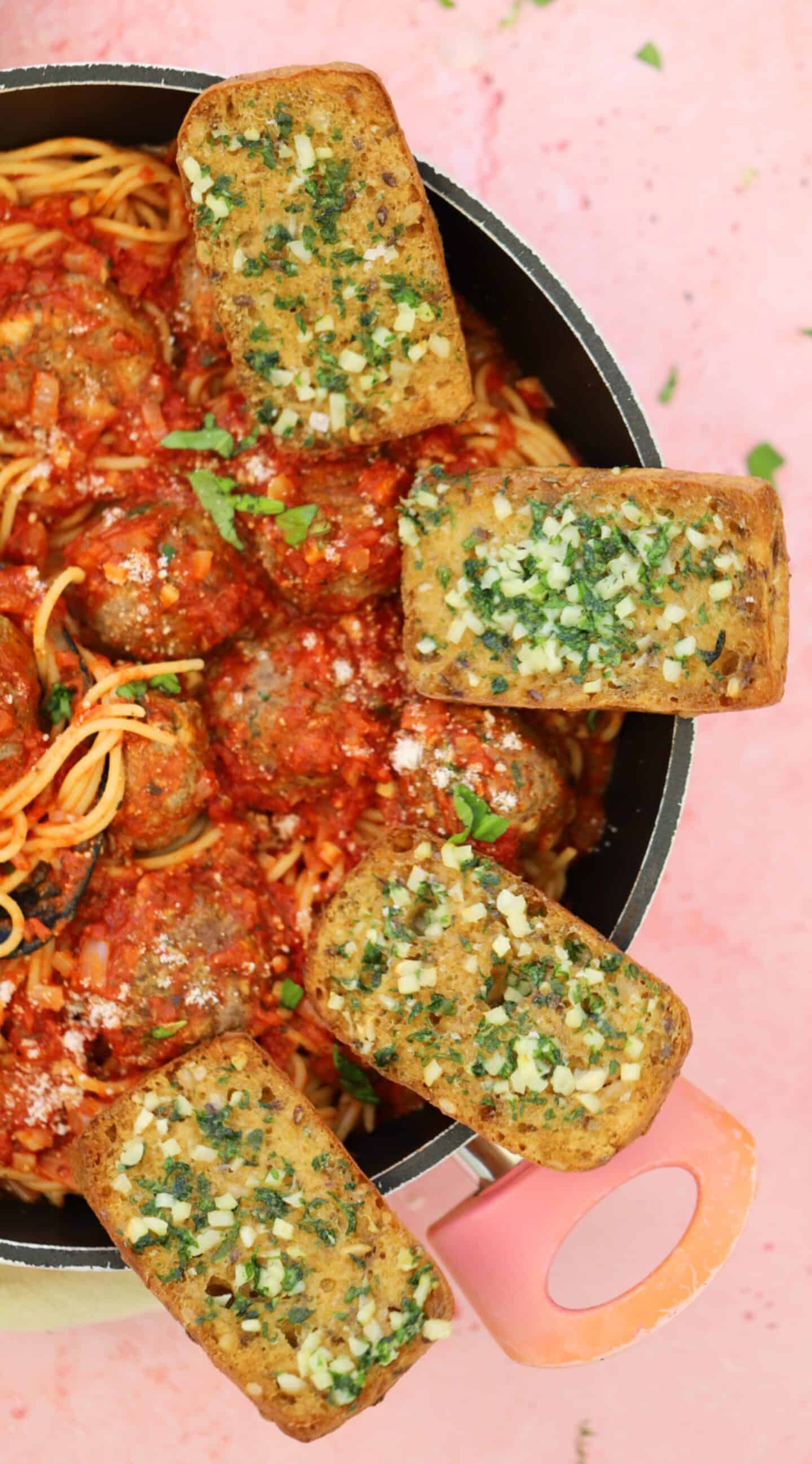 Gluten free garlic bread in a pan with spaghetti and meatballs.