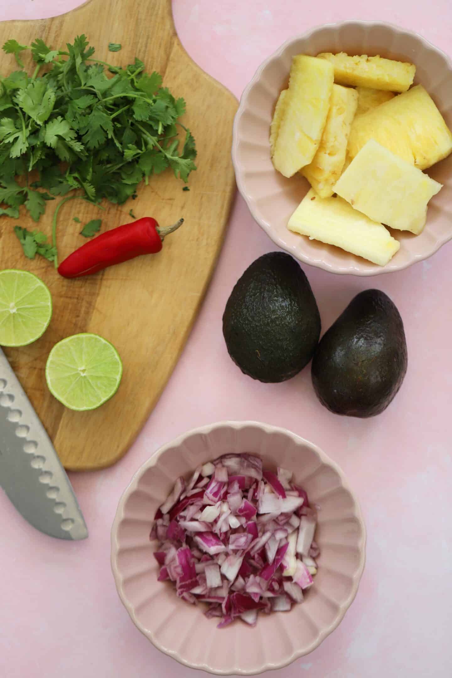 avocado and pineapple salsa ingredients on pink worktop.