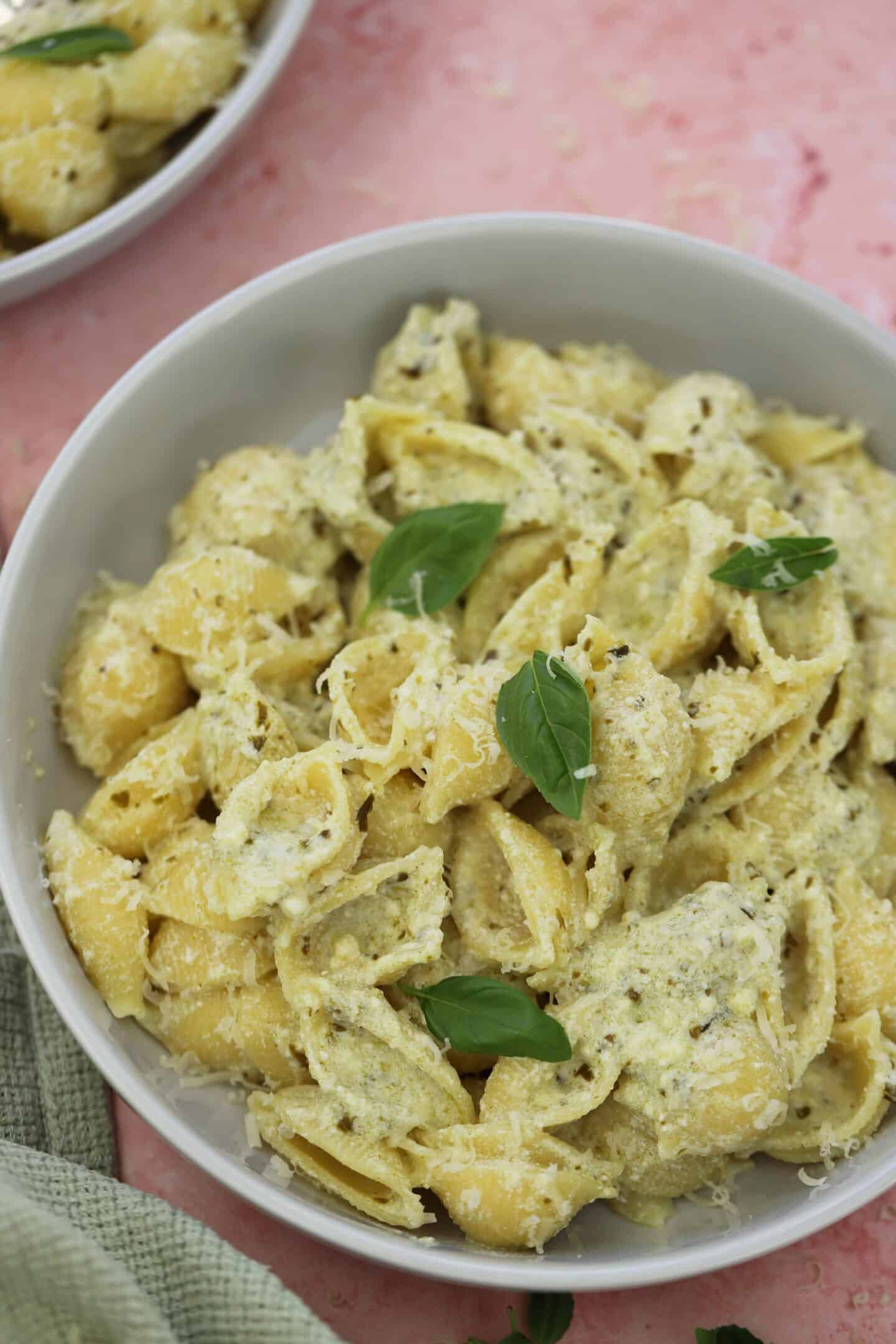 A bowl of pesto and ricotta pasta with basil leaves on top.