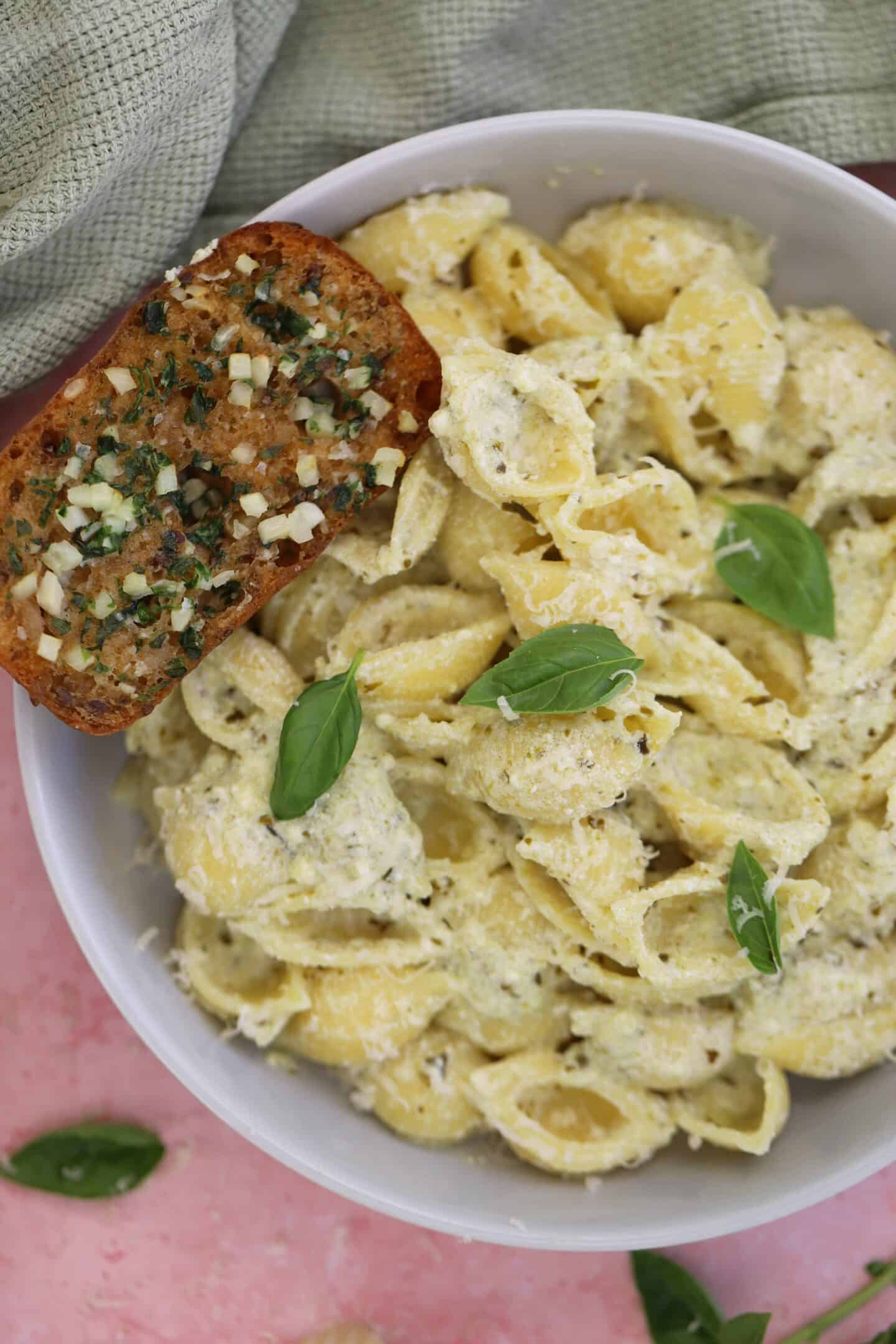 Pesto and ricotta pasta in a bowl with gluten free garlic bread.