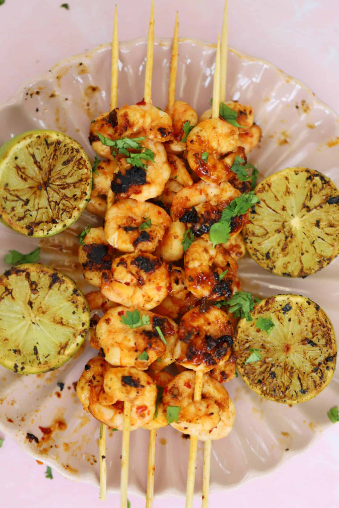 King prawn kebabs on a plate with lime wedges.