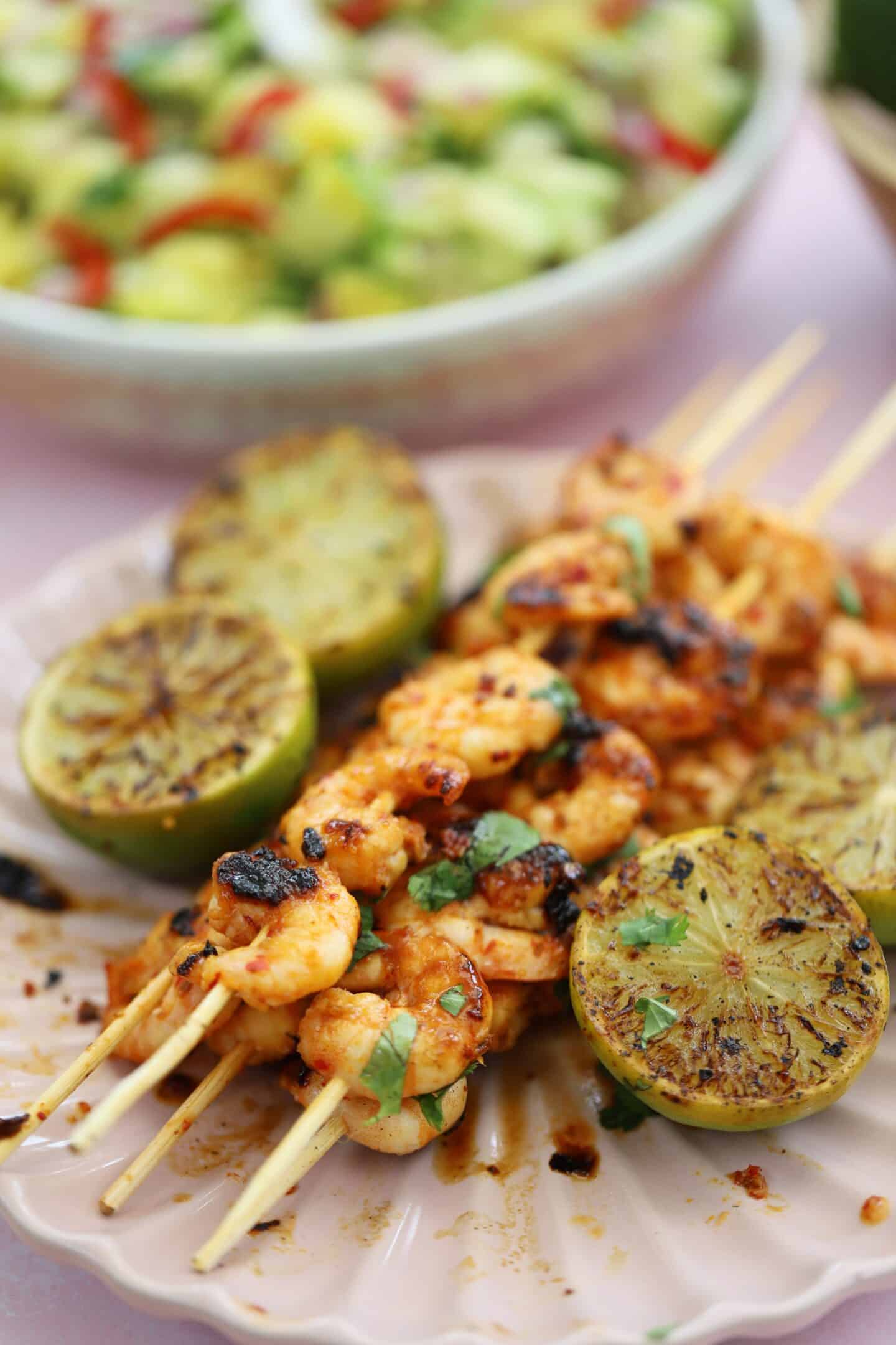 Grilled shrimp skewers with lime wedges and salsa in background.