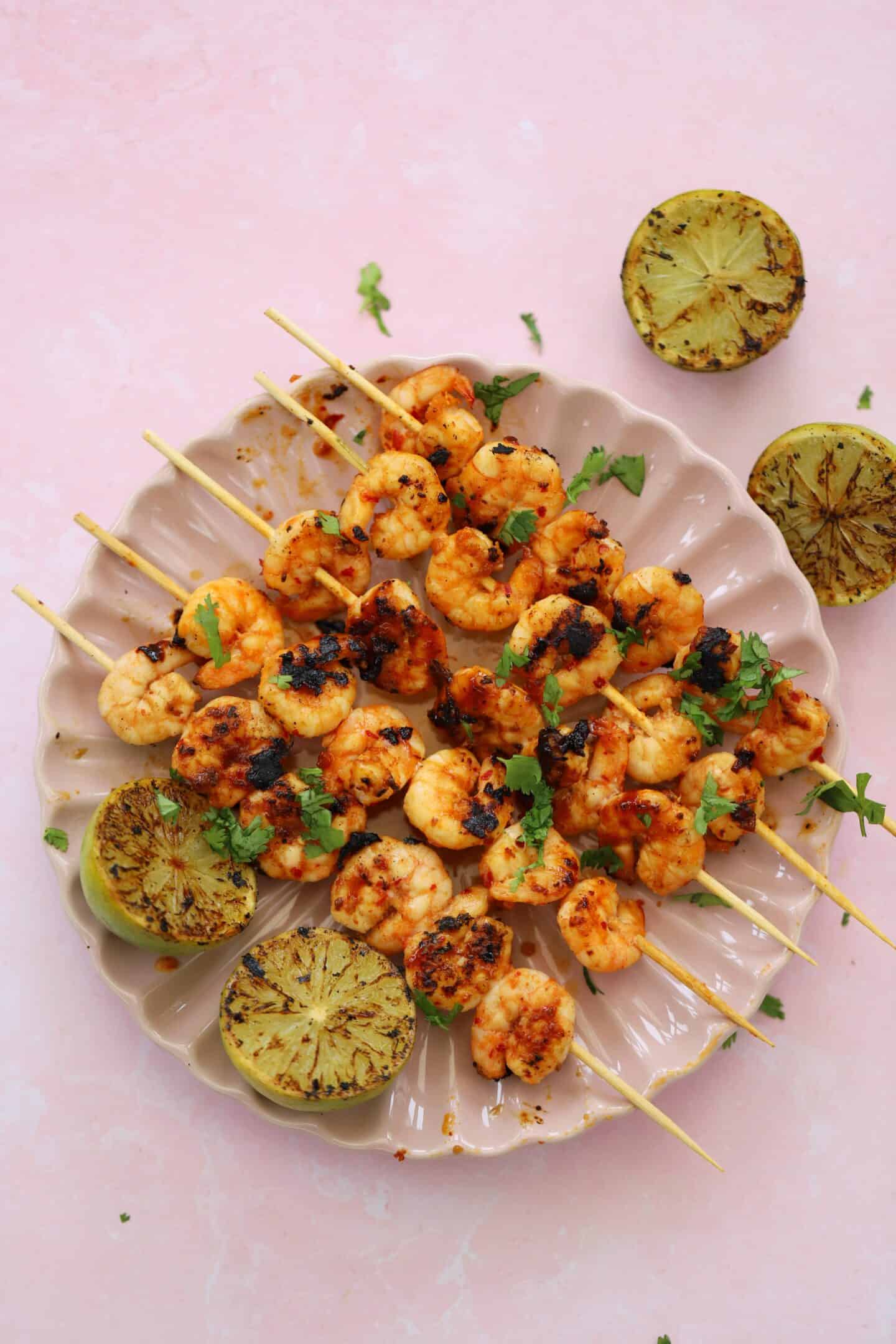 A plate of prawn kebabs with charred lime wedges.