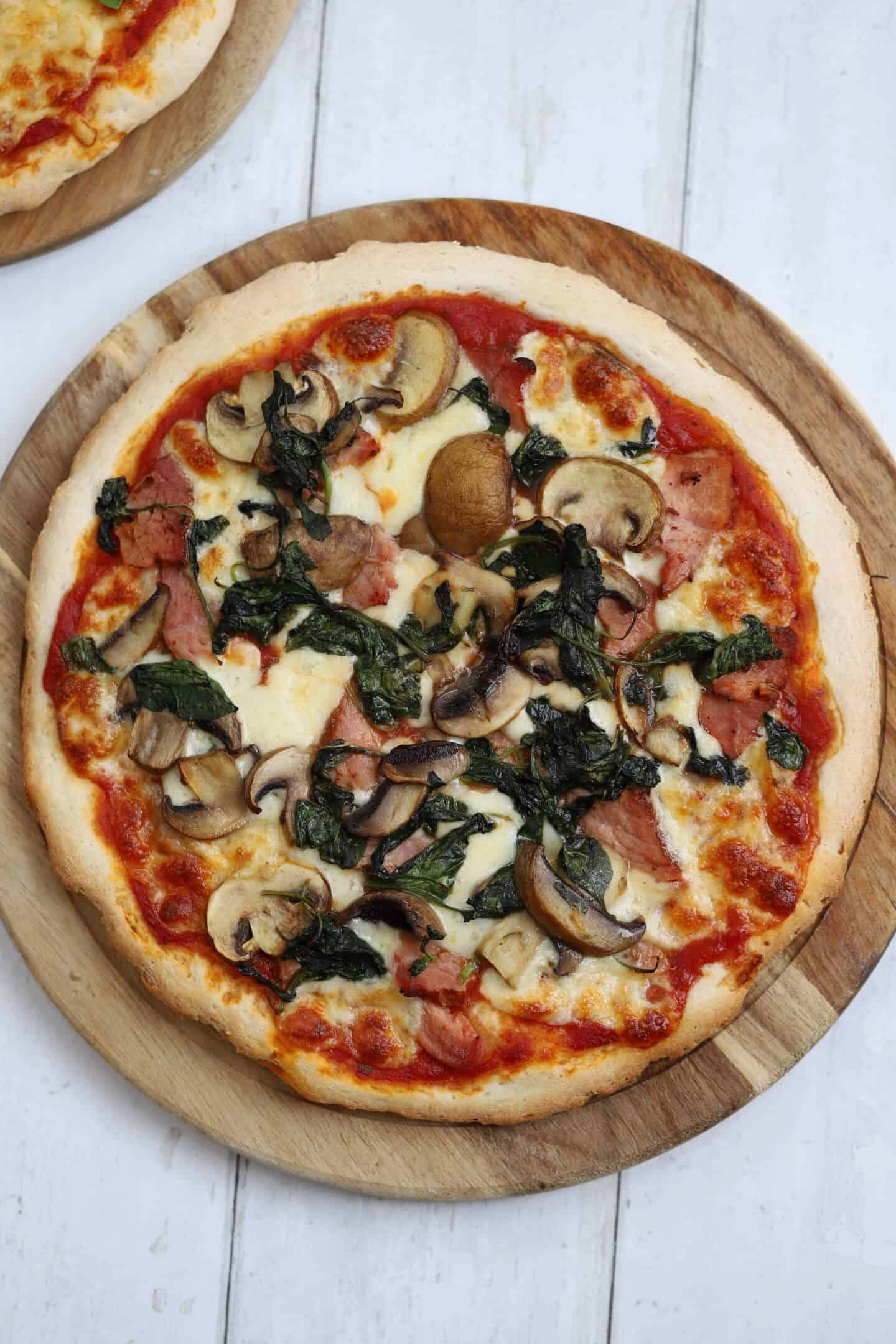 A gluten free ham and mushroom pizza on a board.