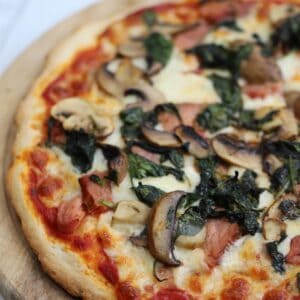 A gluten free pizza with ham, spinach and mushroom.