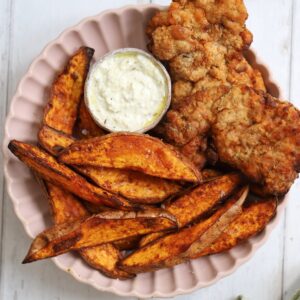 A plate of fried chicken and sweet potato wedges with feta dip.