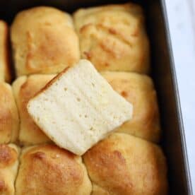 A tray of gluten free Hawaiian rolls with one cut in half on top.