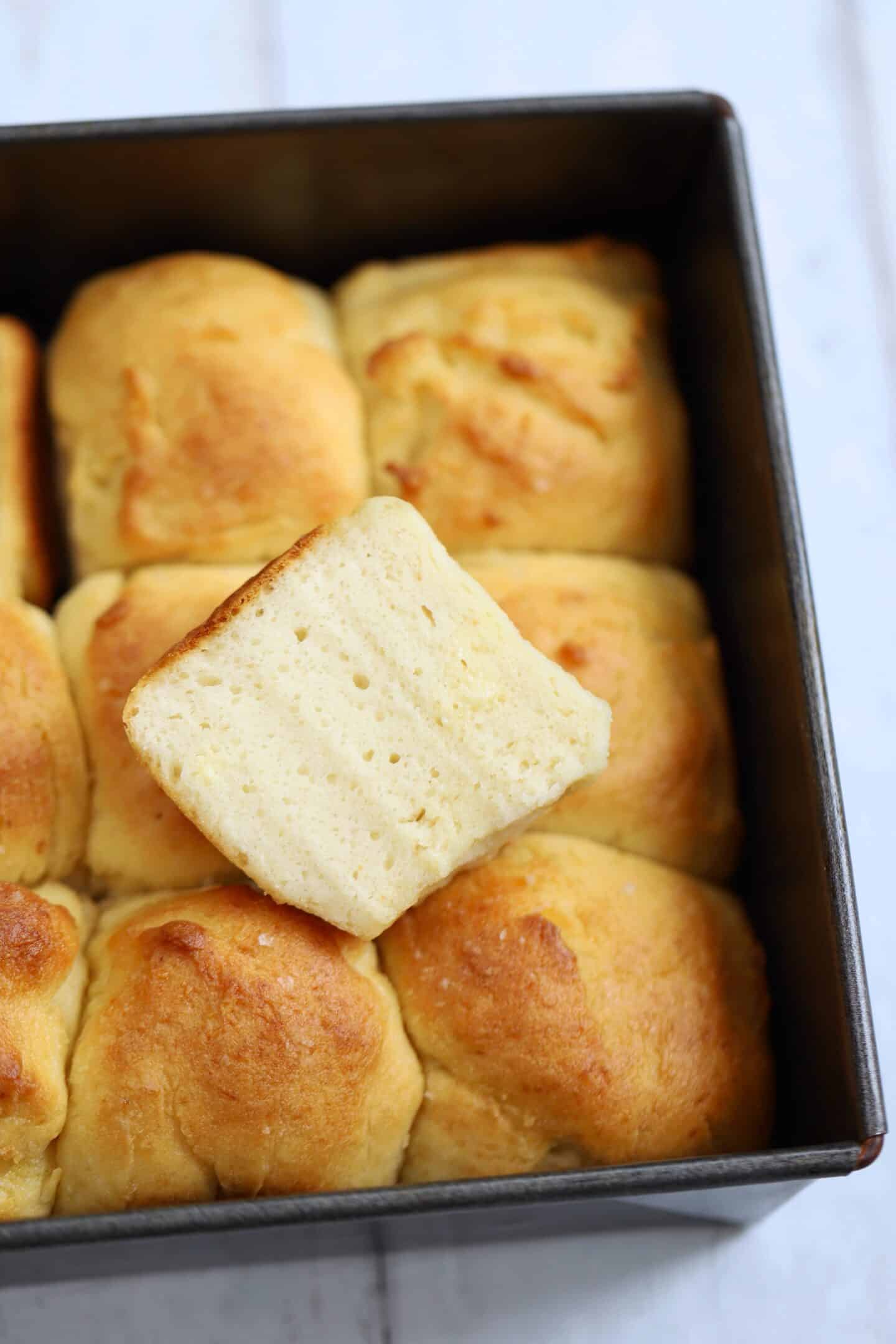 A tray of gluten free Hawaiian rolls with one cut in half on top.