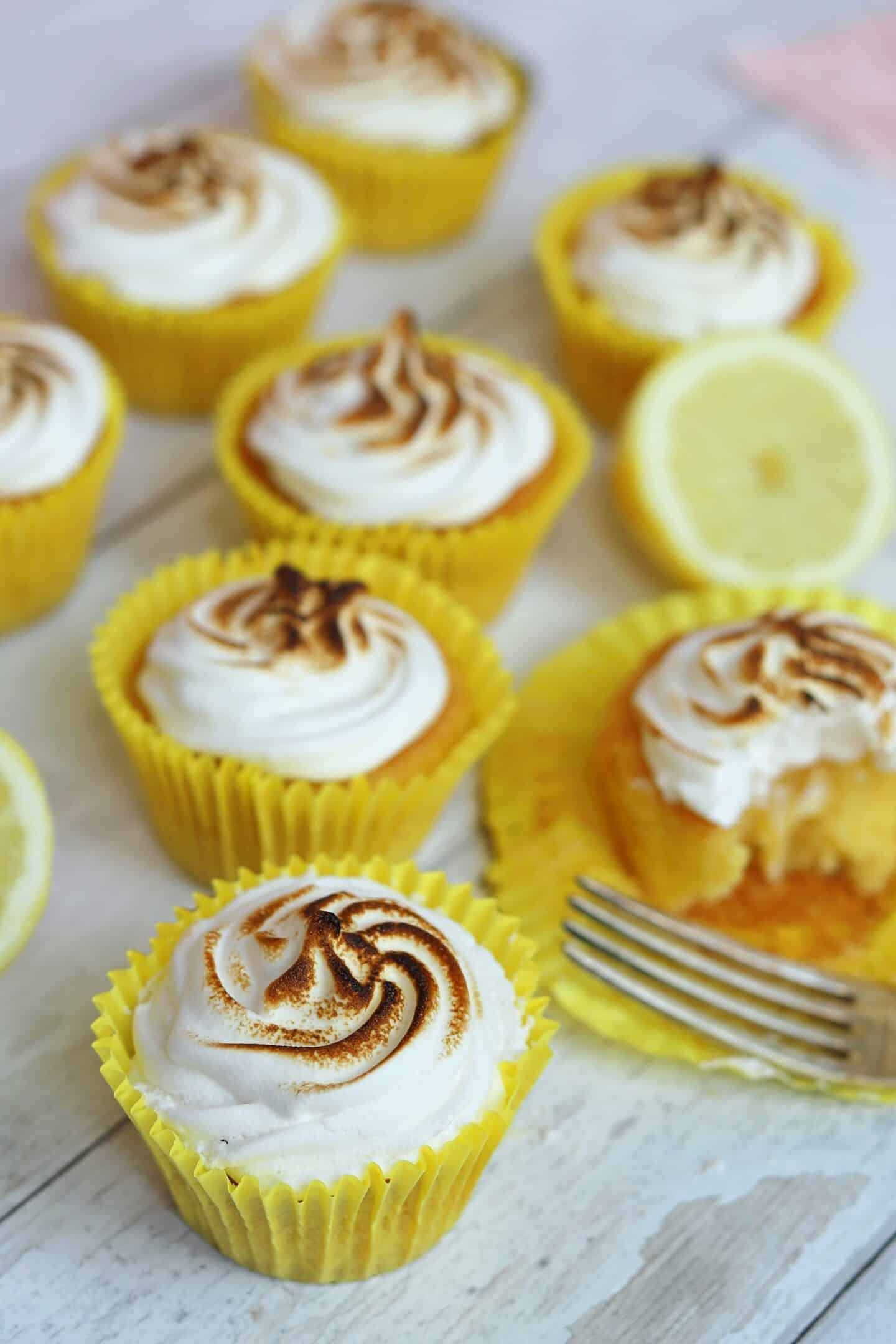Lemon meringue pie cupcakes on a white wooden backdrop.