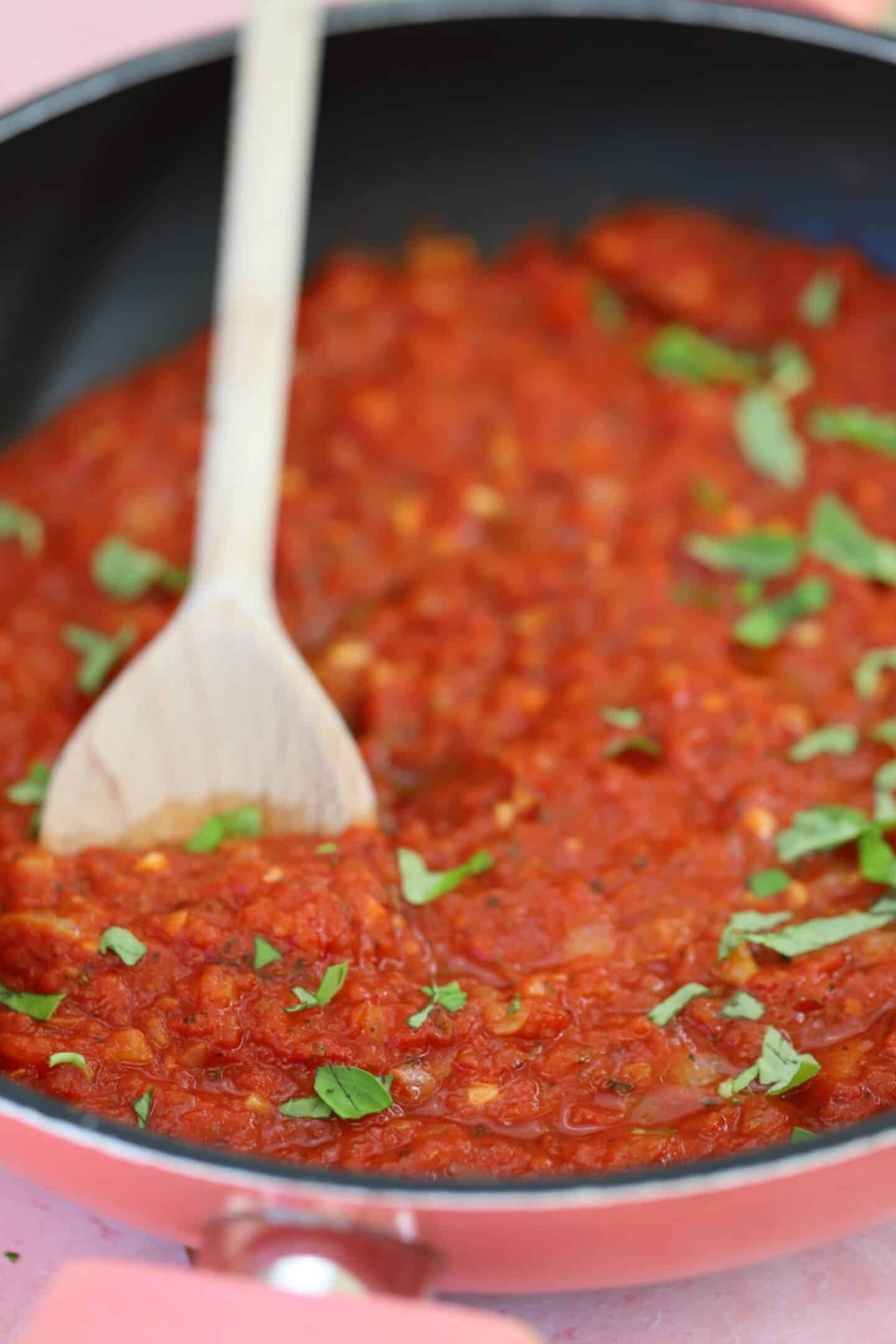 A pan of homemade marinara sauce with a wooden spoon.