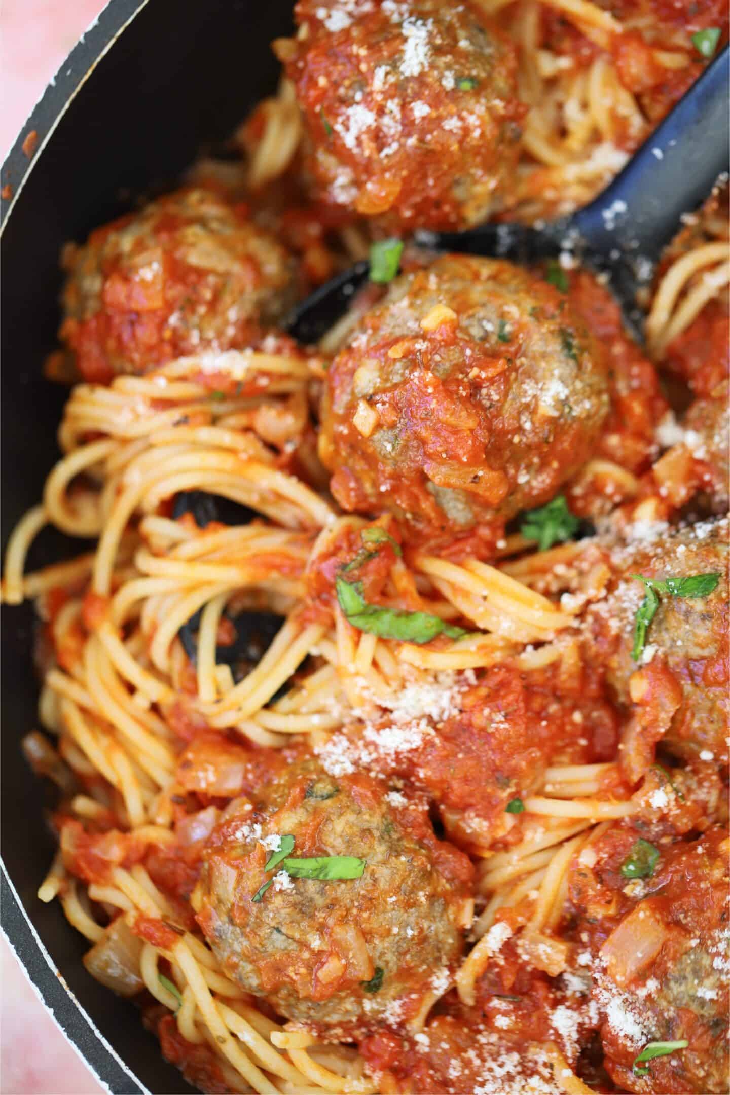 Close up of gluten free meatballs in a pan with sauce and spaghetti.