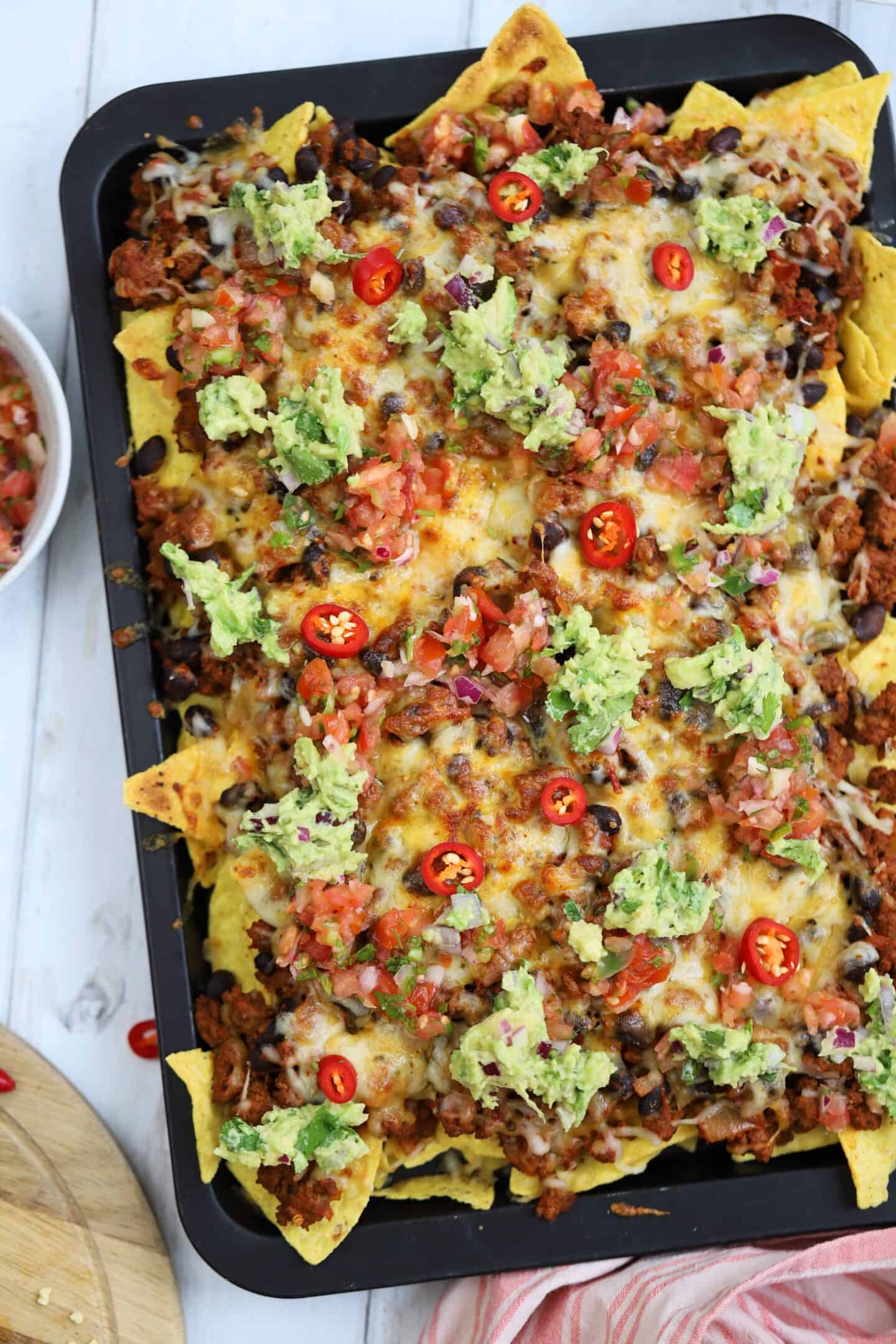 A tray of gluten free nachos with beef, cheese, guacamole and salsa.