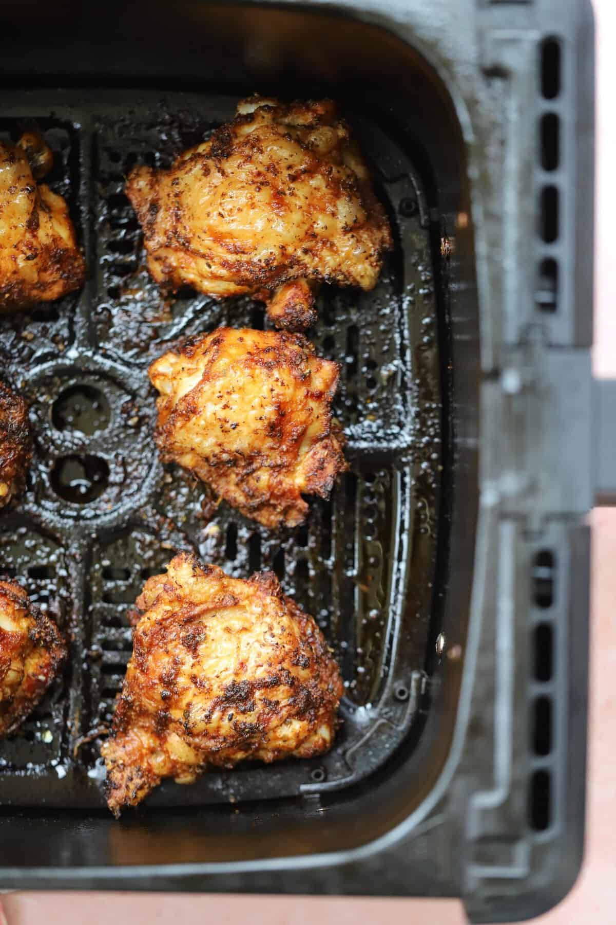 Crispy chicken thighs in an air fryer basket.