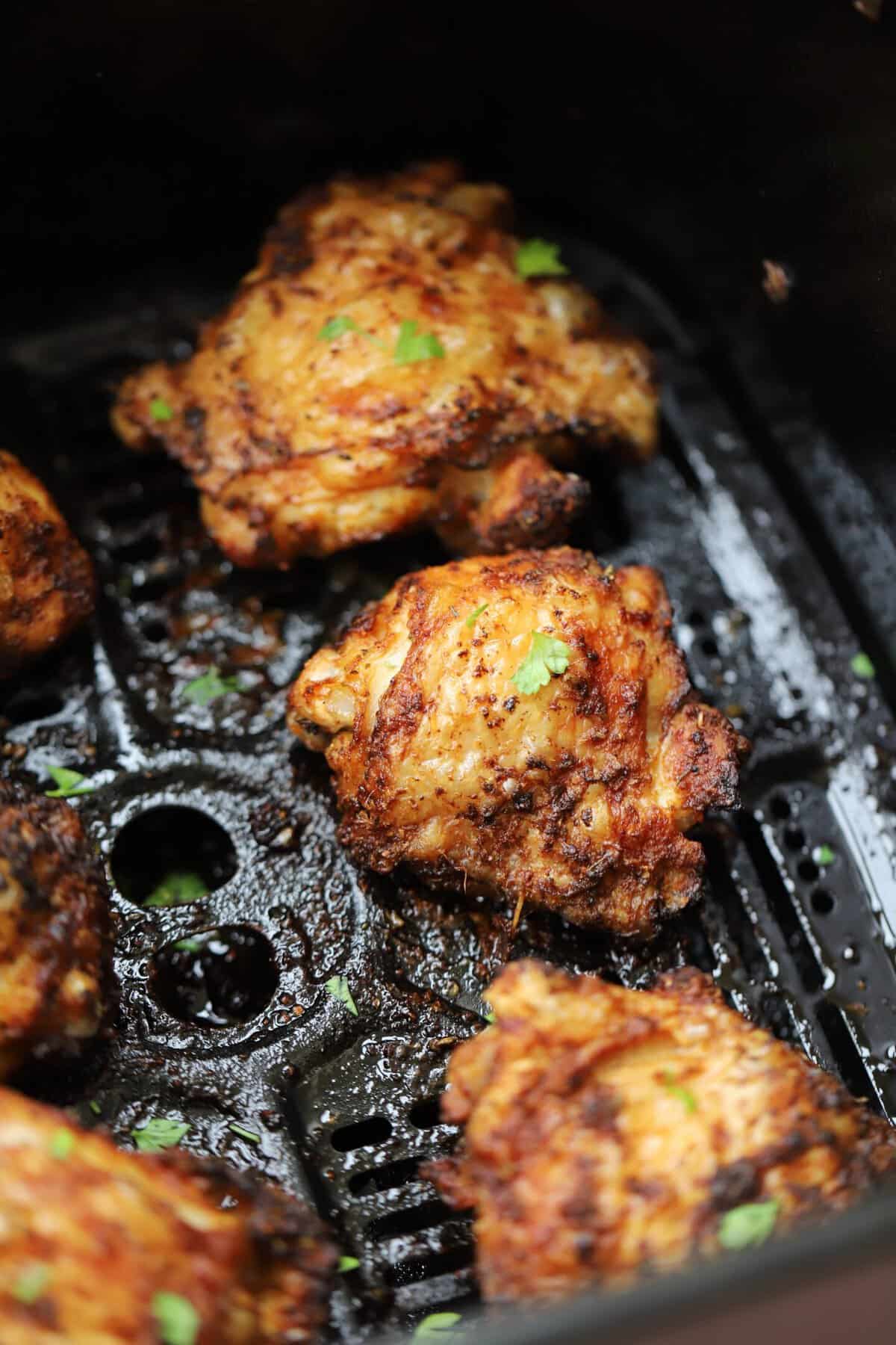 Crispy chicken thighs in an air fryer basket.