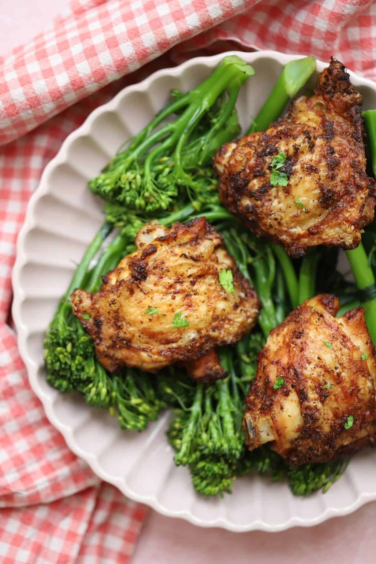 A pink plate with tenderstem broccoli and crispy air fryer chicken thighs on top.