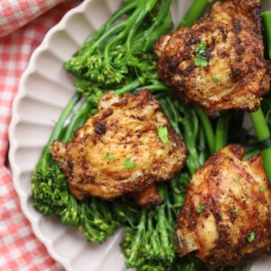 A pink plate with tenderstem broccoli and crispy air fryer chicken thighs on top.