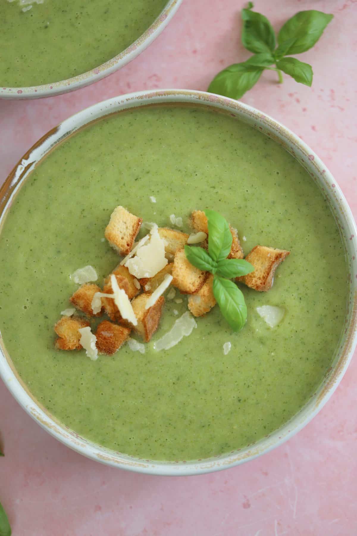 A bowl of gluten free courgette soup with parmesan and basil and gluten free croutons on top.