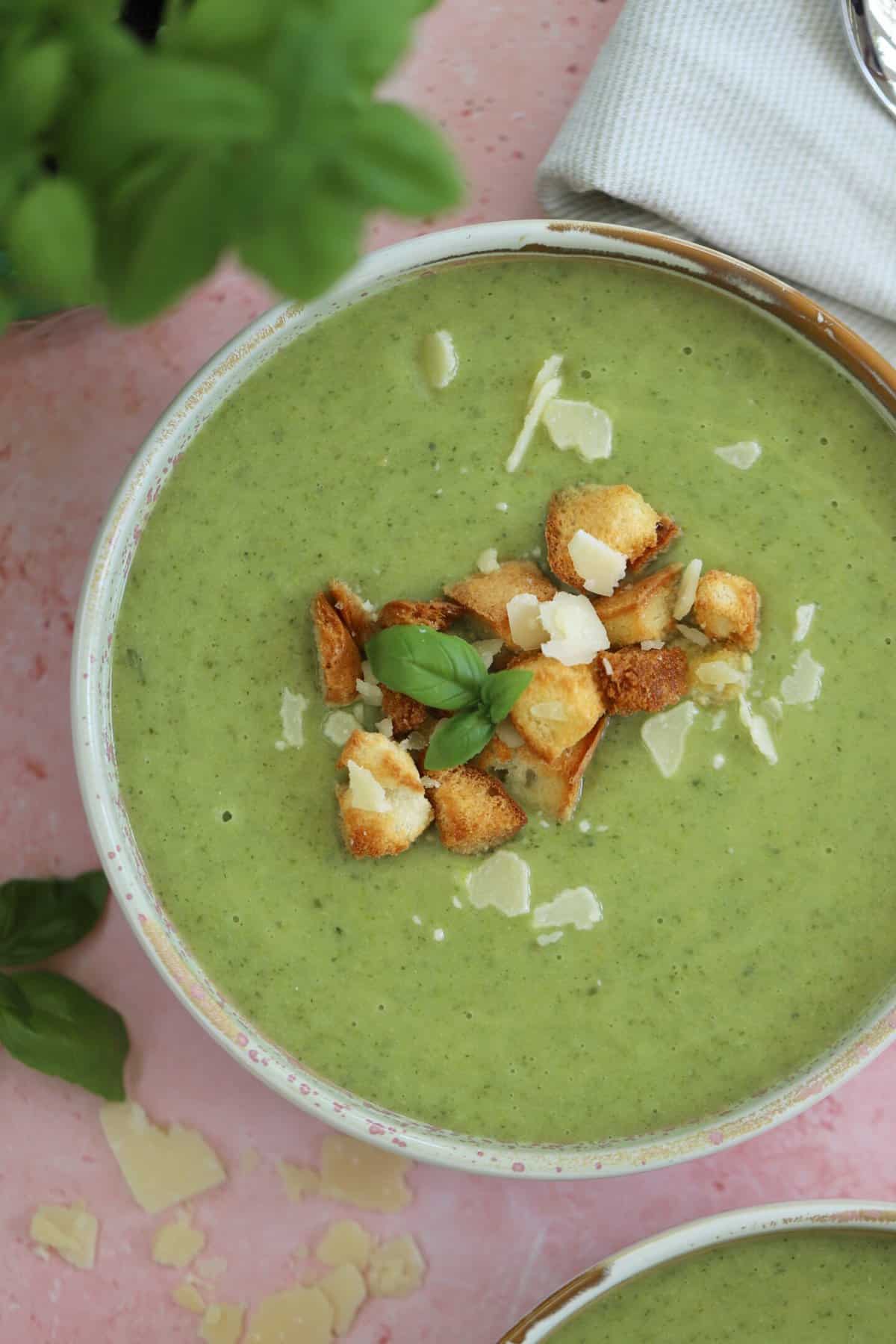 A bowl of gluten free courgette soup with parmesan and basil and gluten free croutons on top.