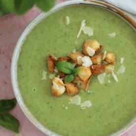 A bowl of gluten free courgette soup with parmesan and basil and gluten free croutons on top.