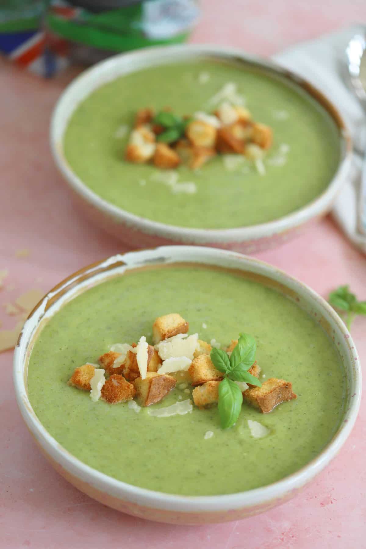 Two bowls of gluten free courgette soup with parmesan and basil and gluten free croutons on top.