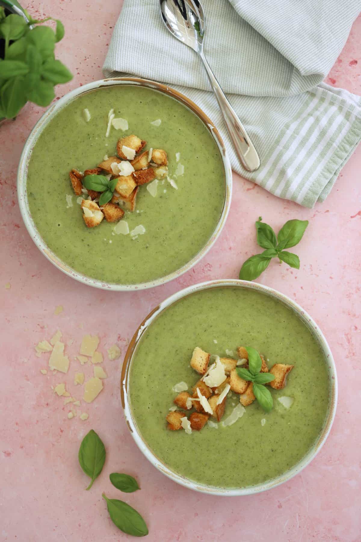 Two bowls of gluten free courgette soup with parmesan and basil and gluten free croutons on top.