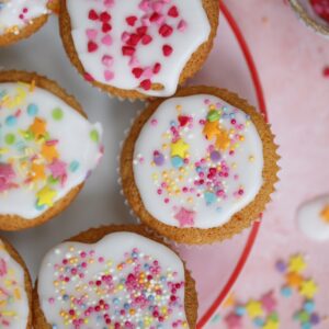 A plate of gluten free fairy cakes with icing and rainbow sprinkles.