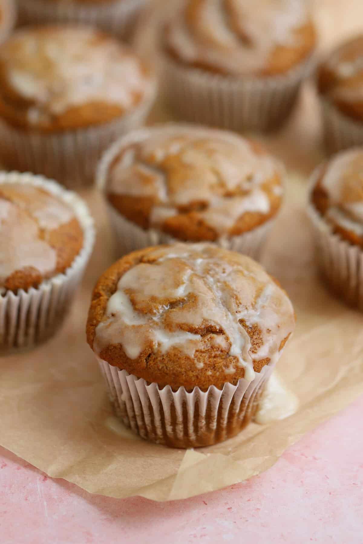 Gluten free pumpkin banana muffins with maple glaze on a sheet of parchment paper.