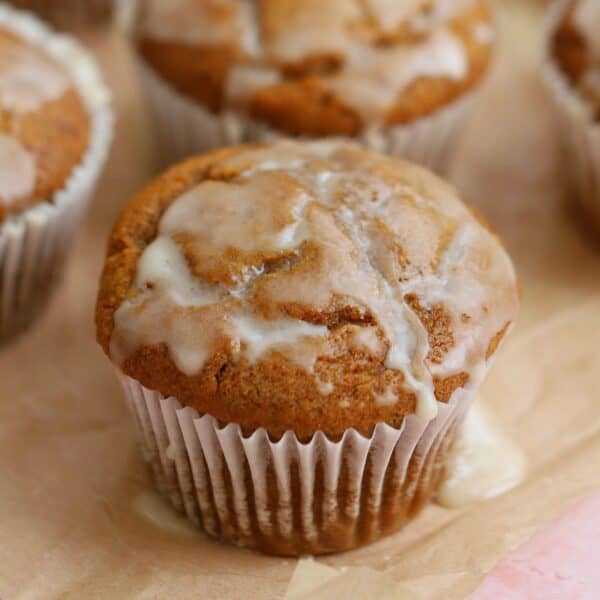 Gluten free pumpkin banana muffins with maple glaze on a sheet of parchment paper.