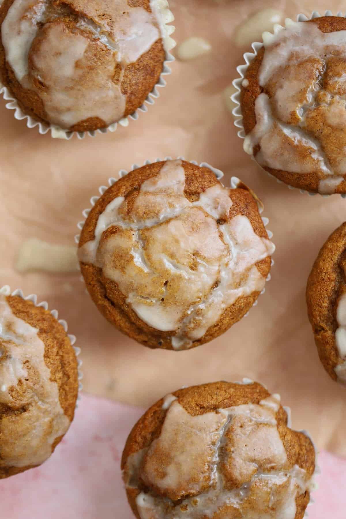 Gluten free pumpkin banana muffins with maple glaze on a sheet of parchment paper.