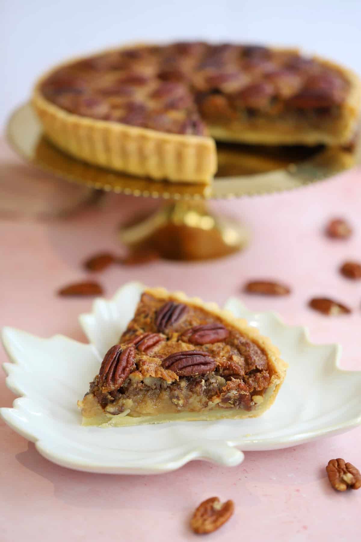 A slice of gluten free pecan pie with pecan pie behind it on a plate.