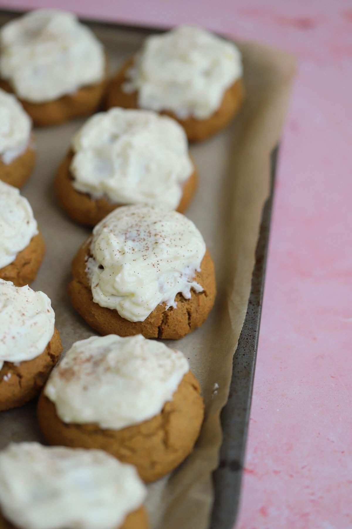 A baking tray with soft gluten free pumpkin cookies and cream cheese frosting.