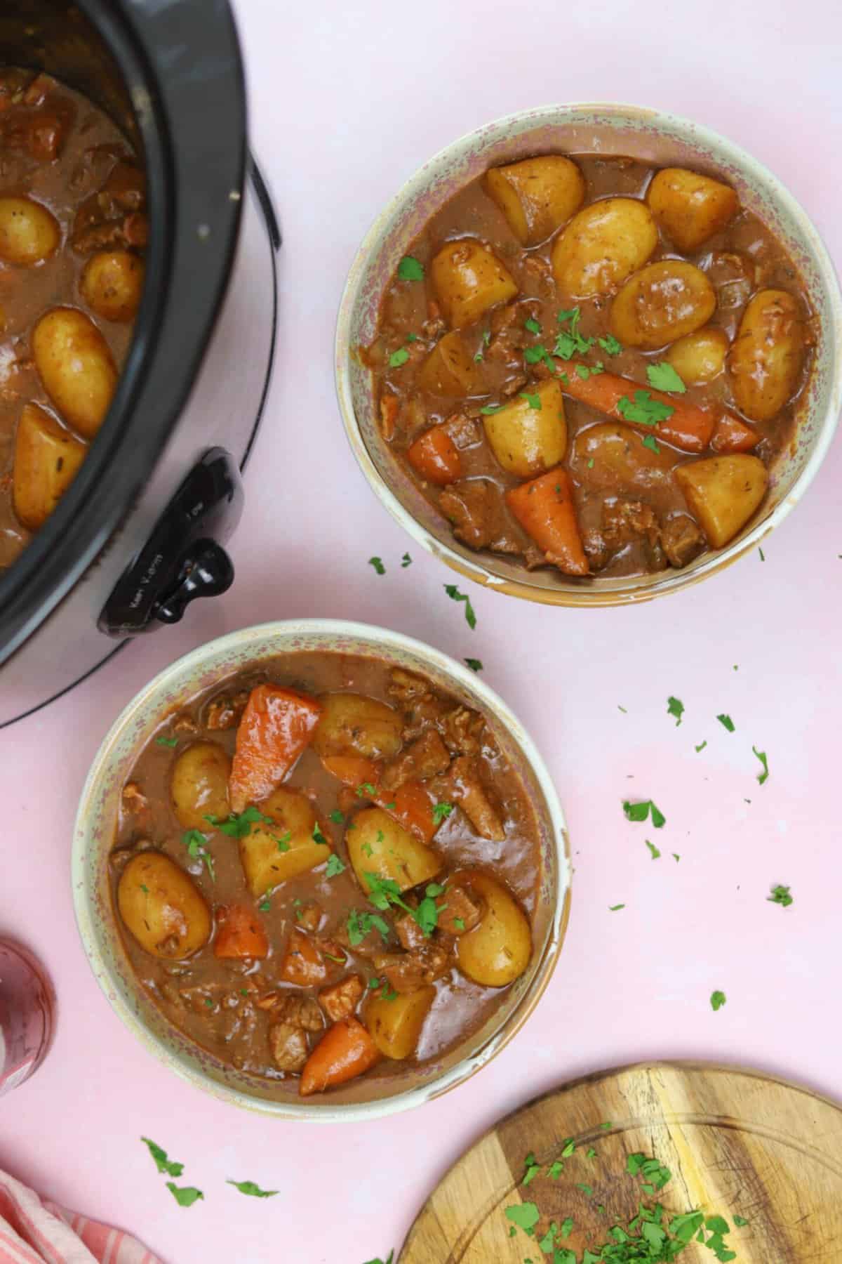 Two bowls of gluten free slow cooker beef and ale stew on a pink worktop.