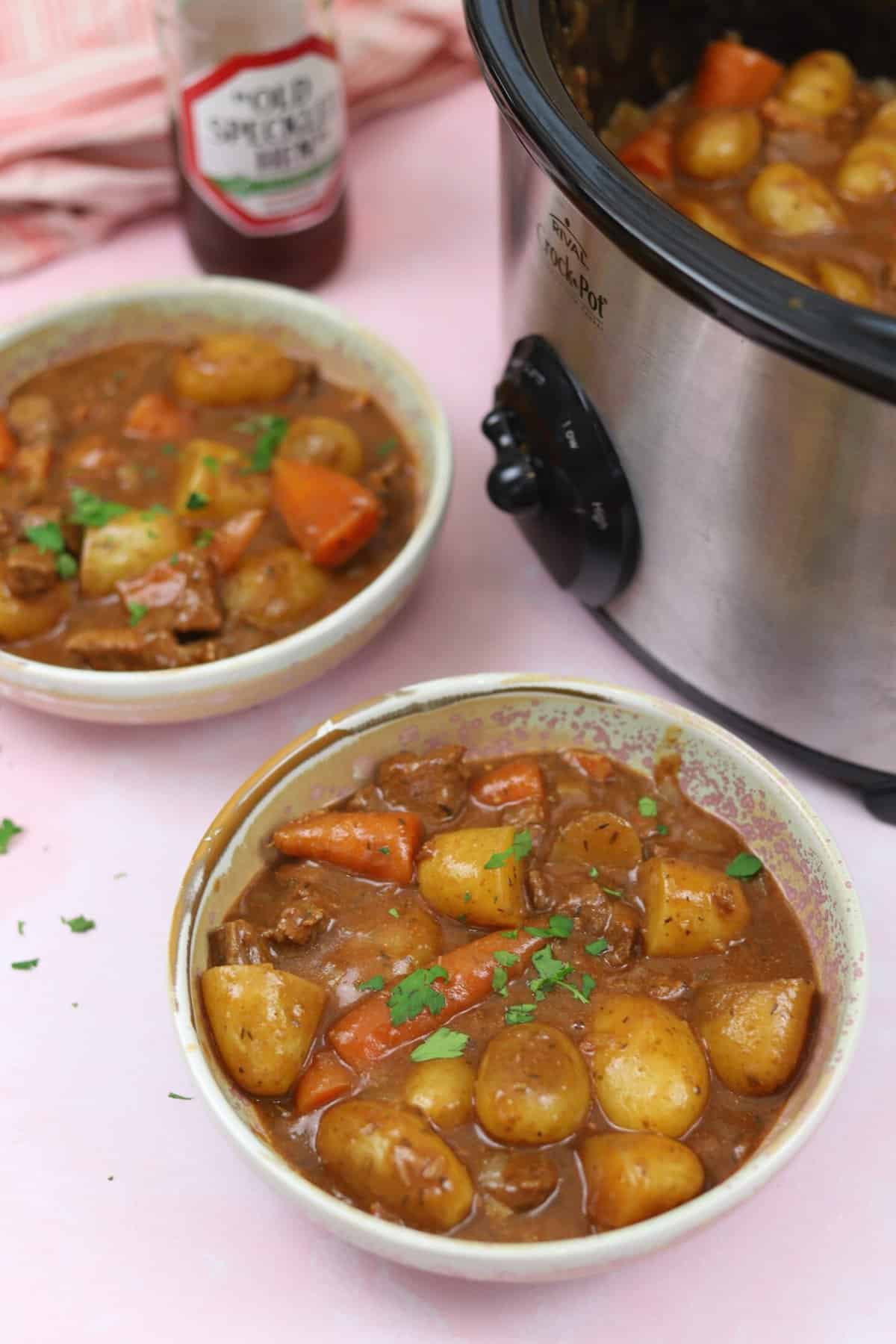 Two bowls of gluten free slow cooker beef and ale stew on a pink worktop.