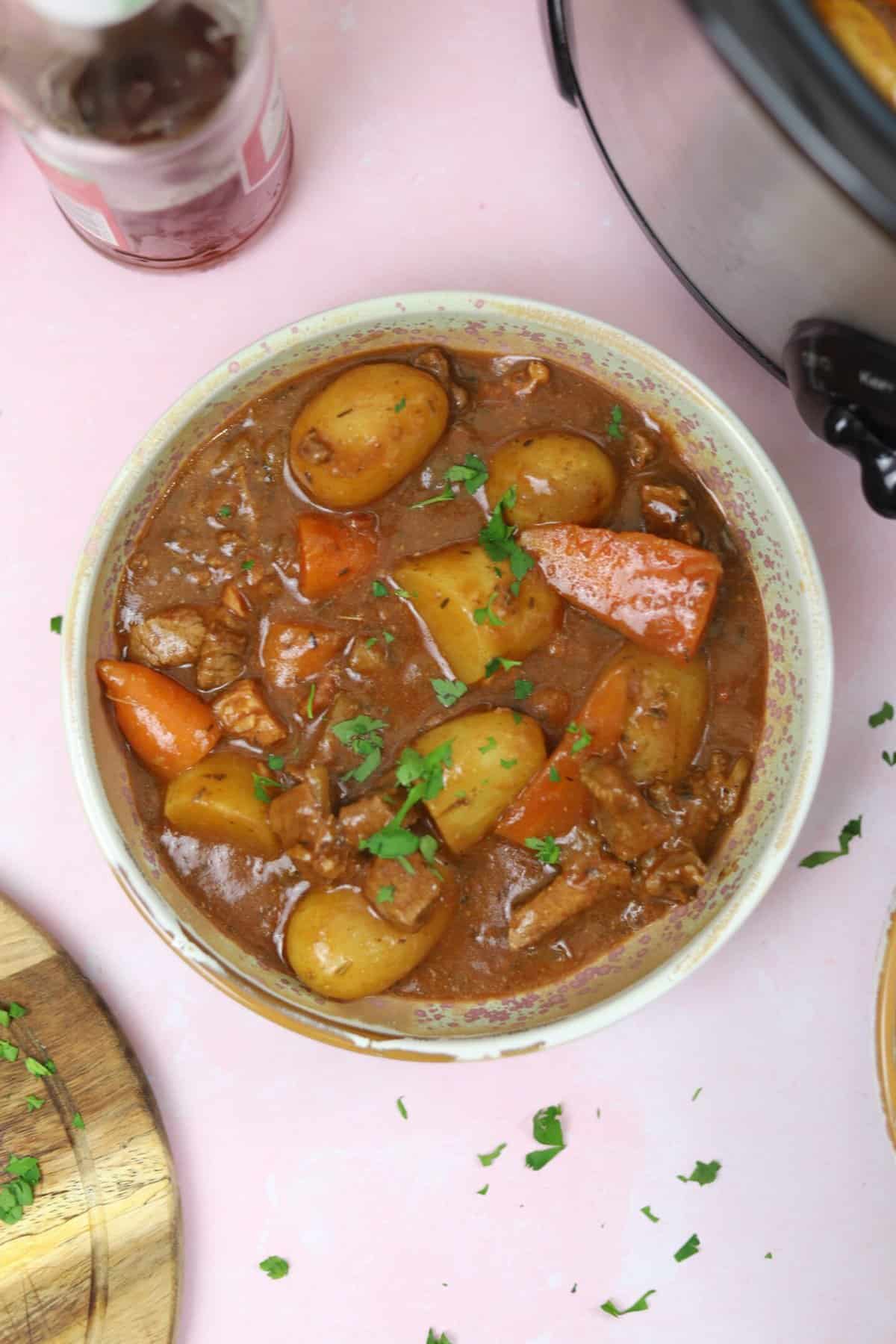 A bowl of gluten free slow cooker beef and ale stew on a pink worktop.