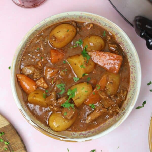 A bowl of gluten free slow cooker beef and ale stew on a pink worktop.