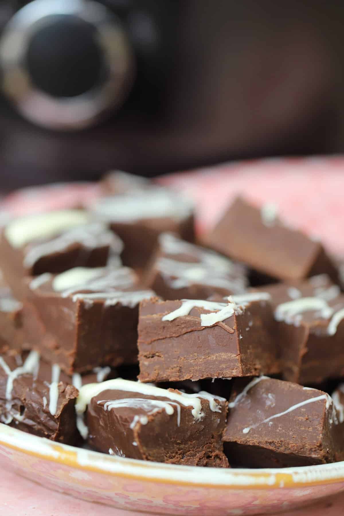 A pile of chocolate fudge in front of a slow cooker on a pink plate.