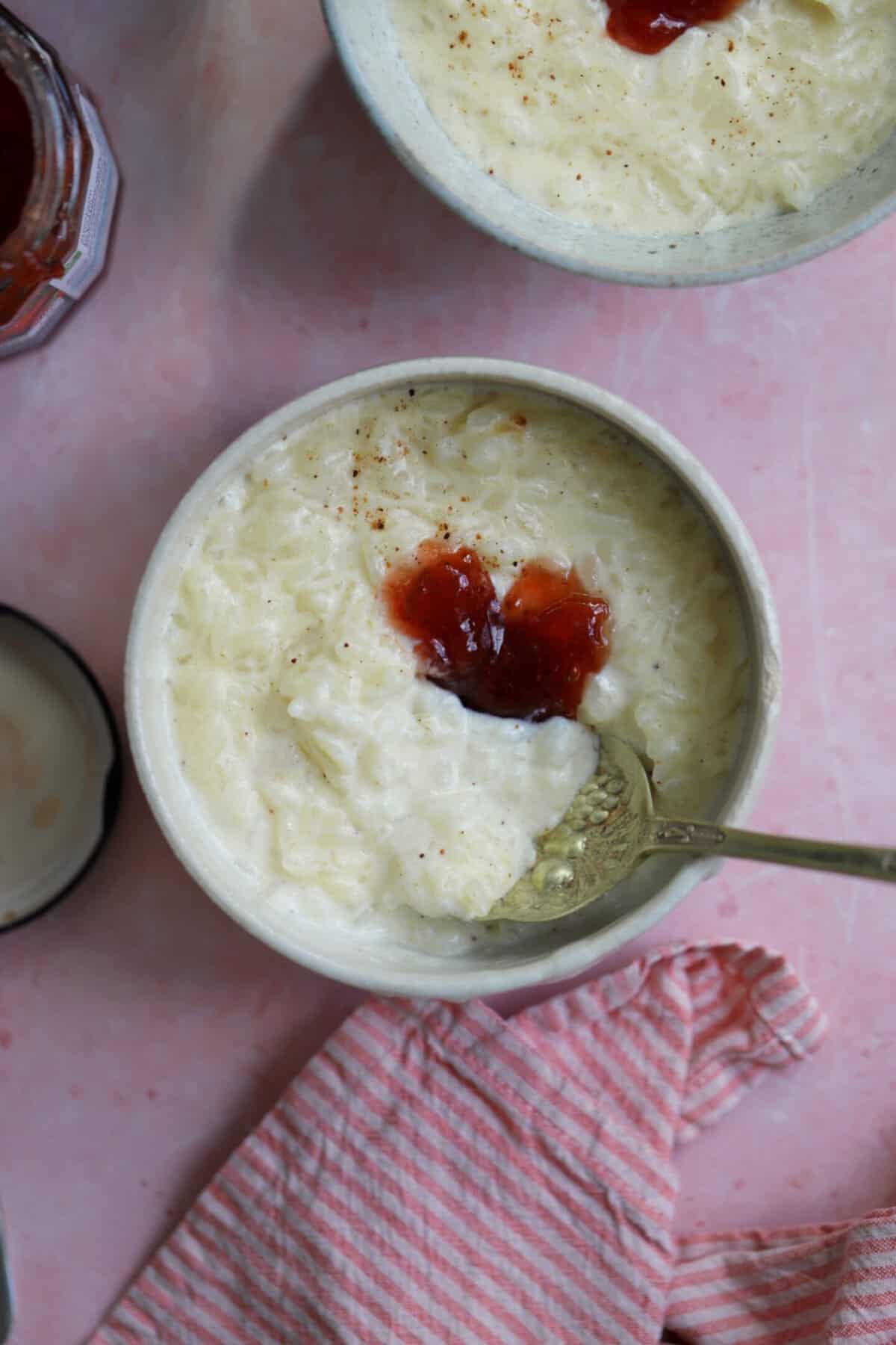 A bowl of slow cooker rice pudding with jam on top and a spoon.