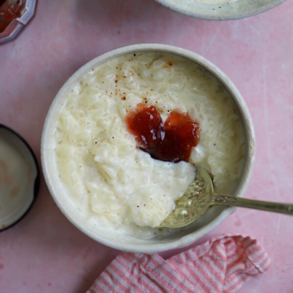 A bowl of slow cooker rice pudding with jam on top and a spoon.