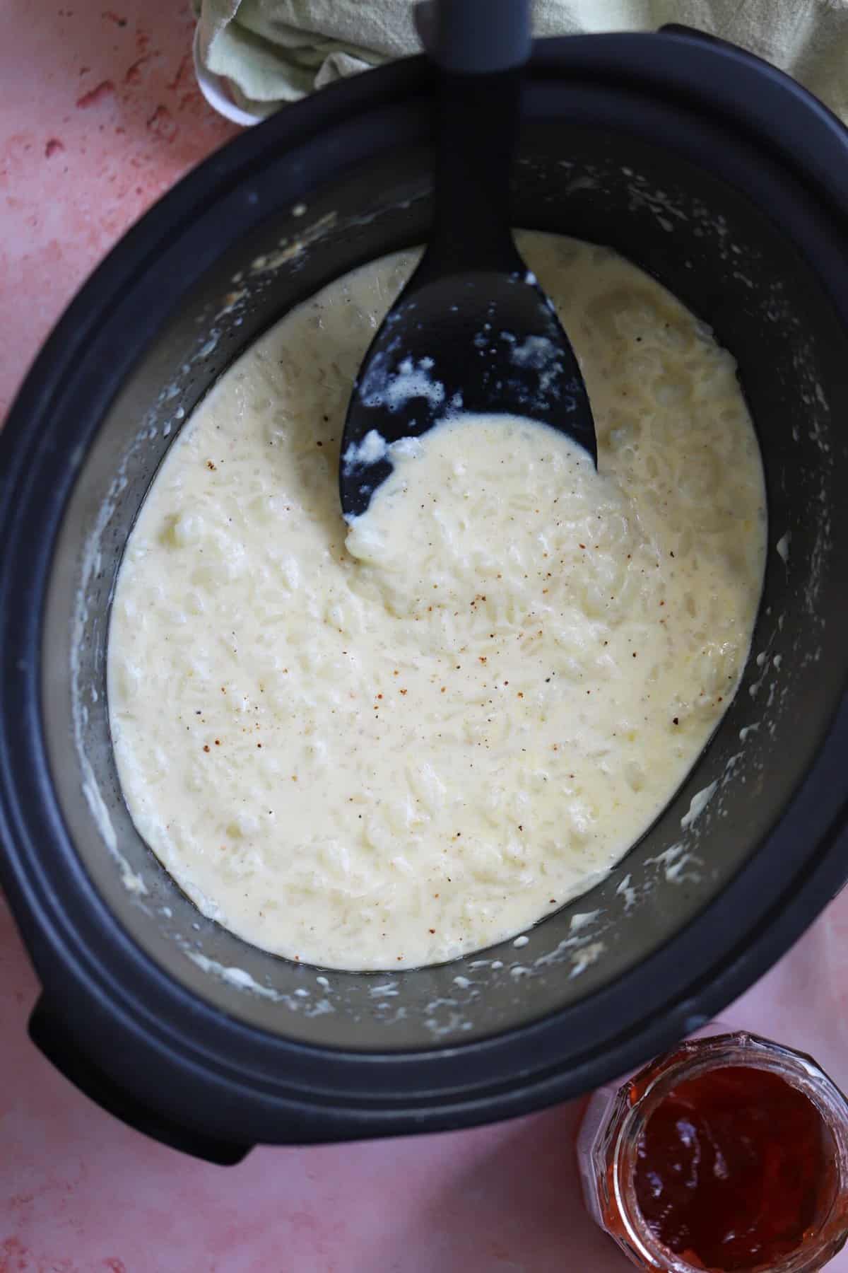 Rice pudding in a slow cooker with a black serving spoon.