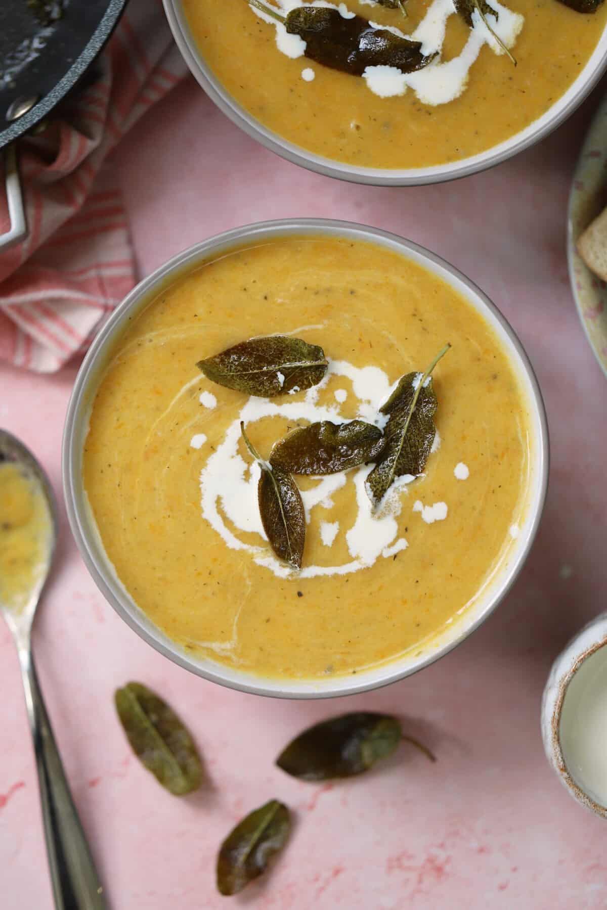 A bowl of winter vegetable soup swirled with cream and topped with crispy sage leaves.