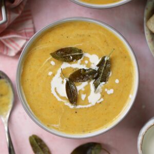 A bowl of winter vegetable soup swirled with cream and topped with crispy sage leaves.