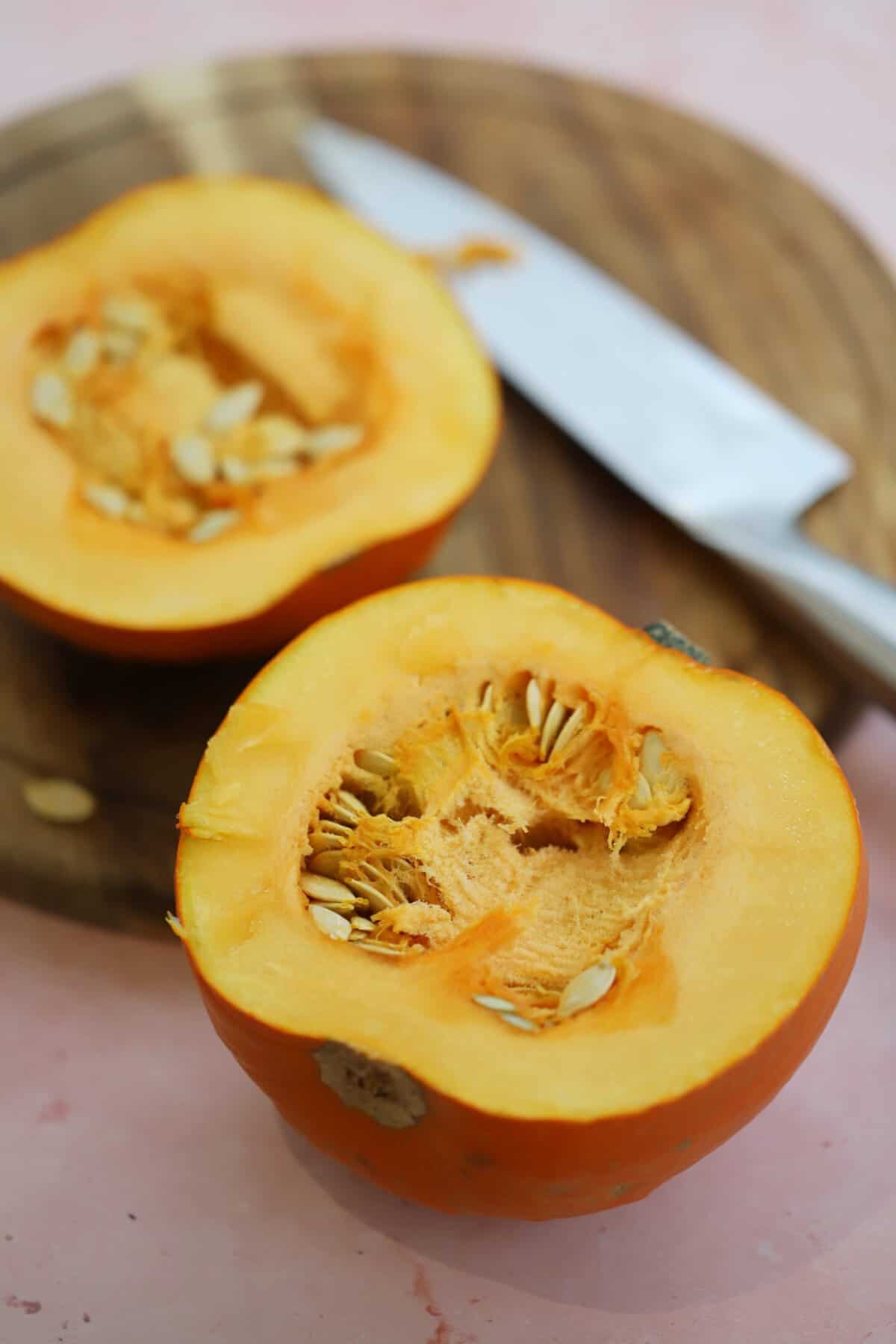 A pumpkin cut in half, flesh-side-up on a chopping board.